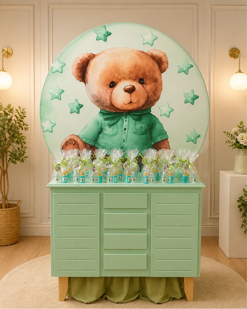 Painel sublimado de ursinho de blusa verde atrás da mesa de lembrancinhas